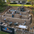 Professional crew building stone block retaining wall on sloped yard